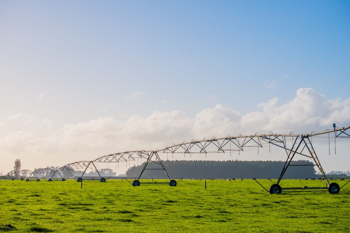 Agriculture modern irrigation. watering spray machine set on the green grassland field with blue sky and warm light scene.